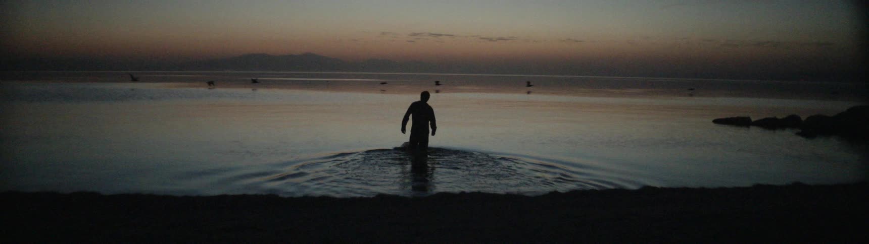 A man walks into the shore at sunset