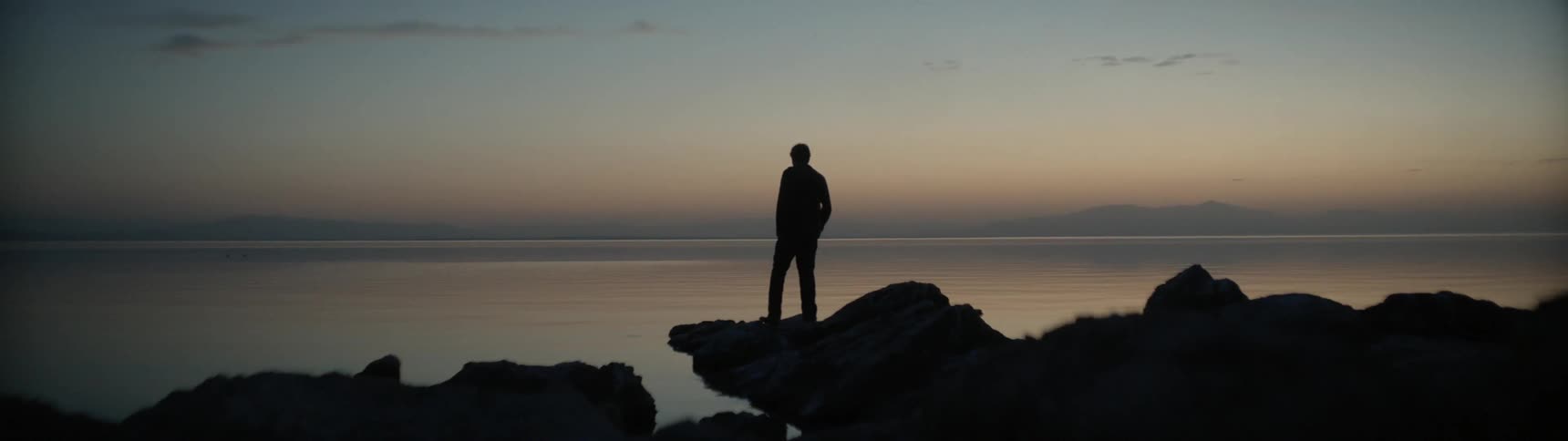 A man walks on a lakeshore at sunrise