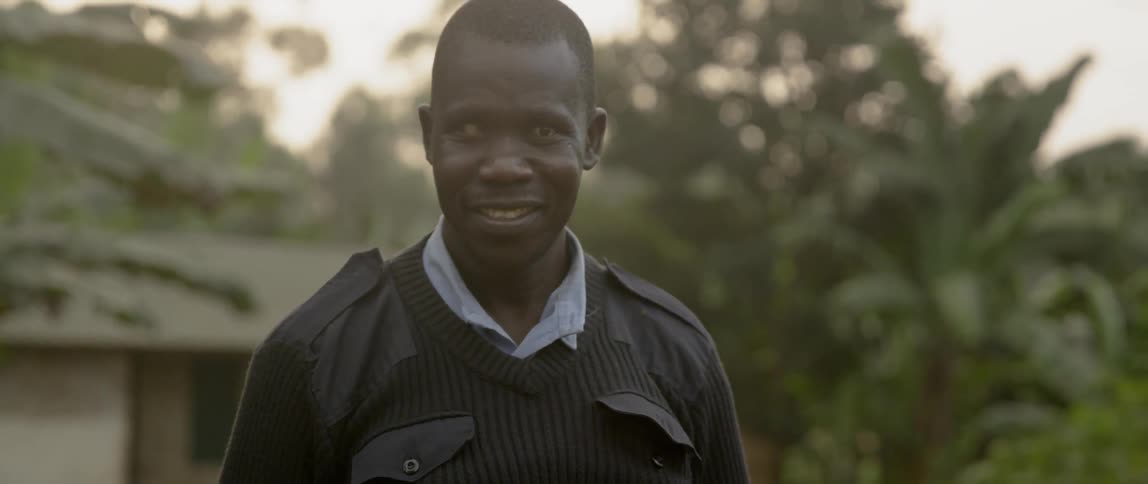 Man stands outside near a house and trees smiling