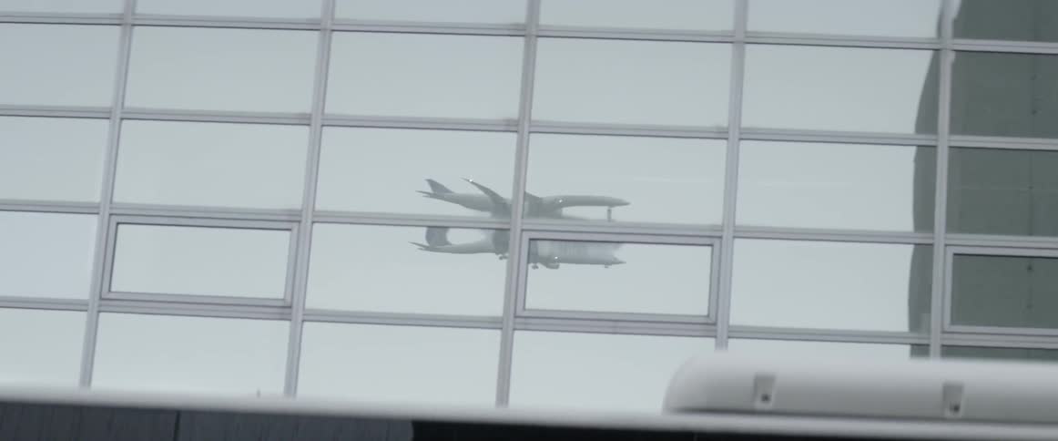 A reflection of a plane flying in the glass of a building