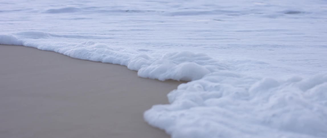 Waves hitting a sandy shore and forming bubbles