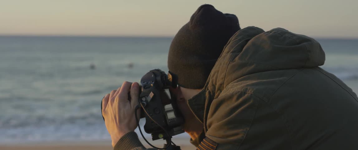 A white man on a beach filming with a camera