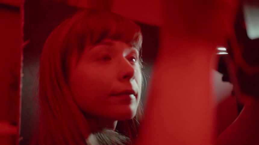 A woman holds something up and looks at it in a red lit room