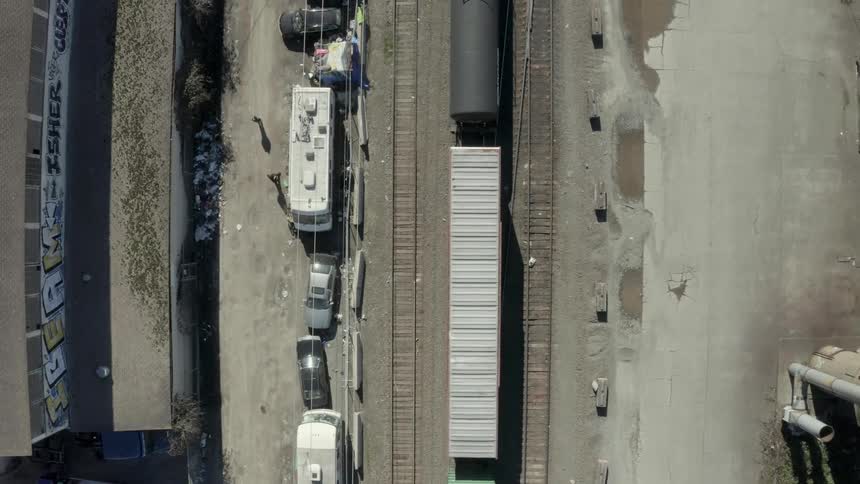 Train travels slowly on the tracks next to homeless camp