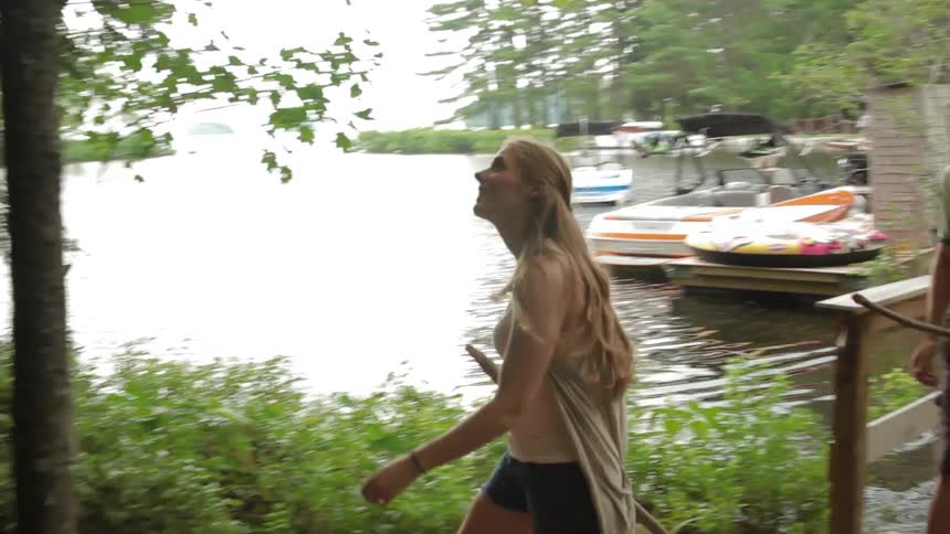A young man and woman walk across a small wooden bridge and along a trail next to a lake