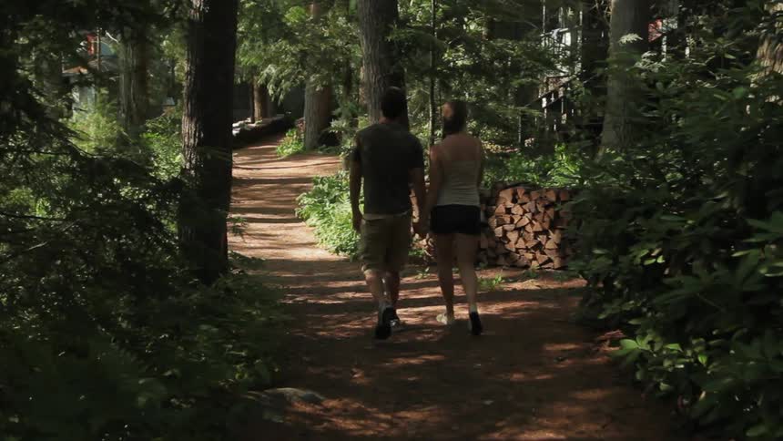 Man and women hold hands as they walk down a trail in the woods