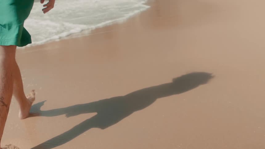 Man is walking on ocean beach on sunny day