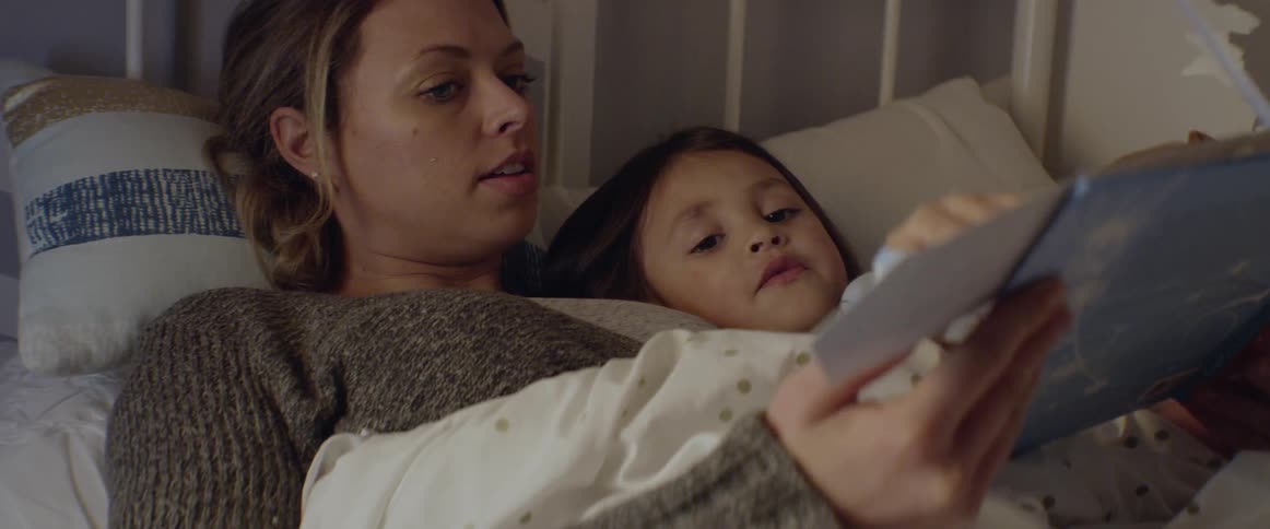 Mother reads story to daughter as they lay in bed