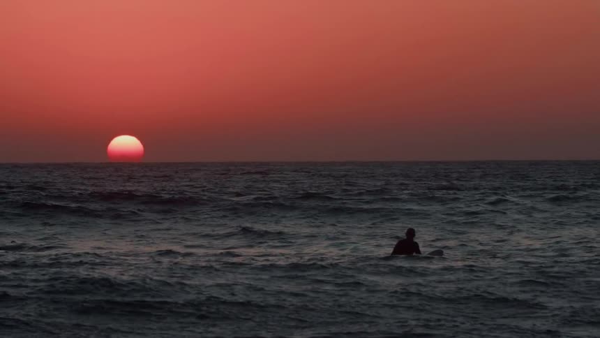 Person sits on a surfboard paddling in the ocean