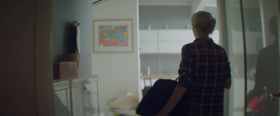 A blonde woman carries a black duffle bag down a bright hallway.