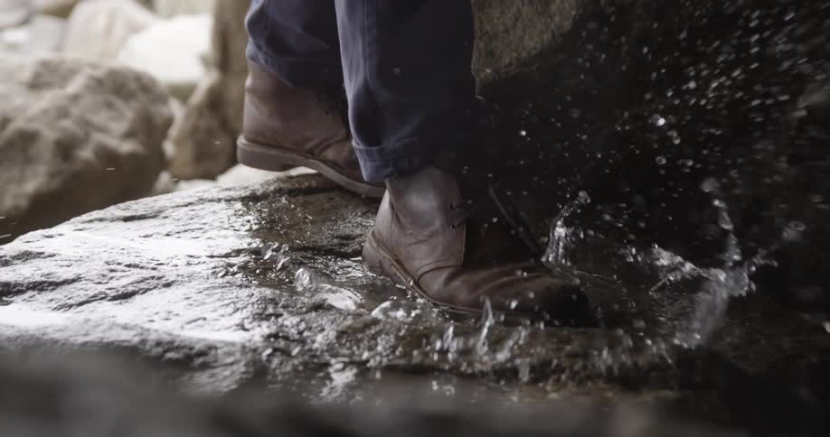A man is walking across watered boulders