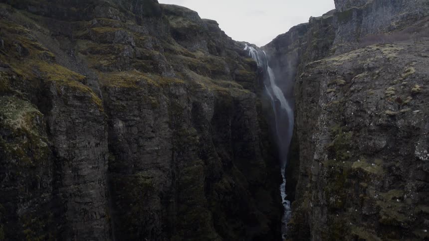 Waterfall flows down mossy rock cliff
