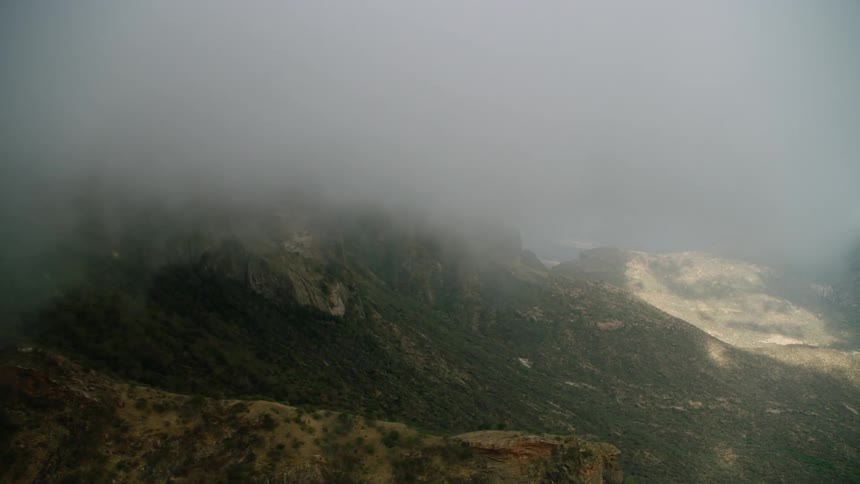Storm clouds are drifting across a mountain range during the day