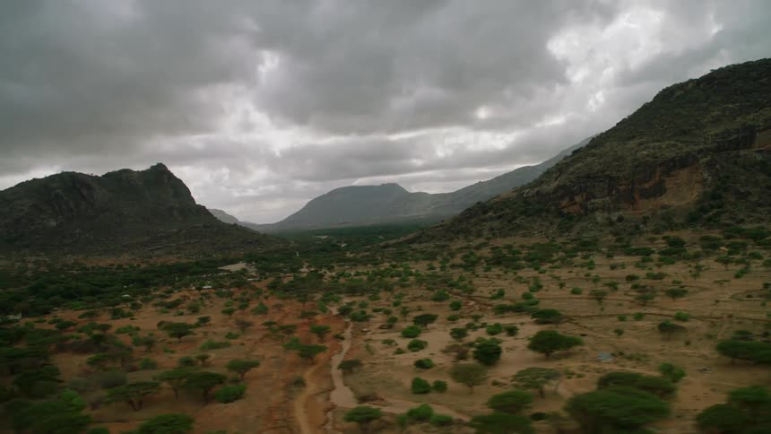 Clouds hang over a landscape with trees and muddy streams