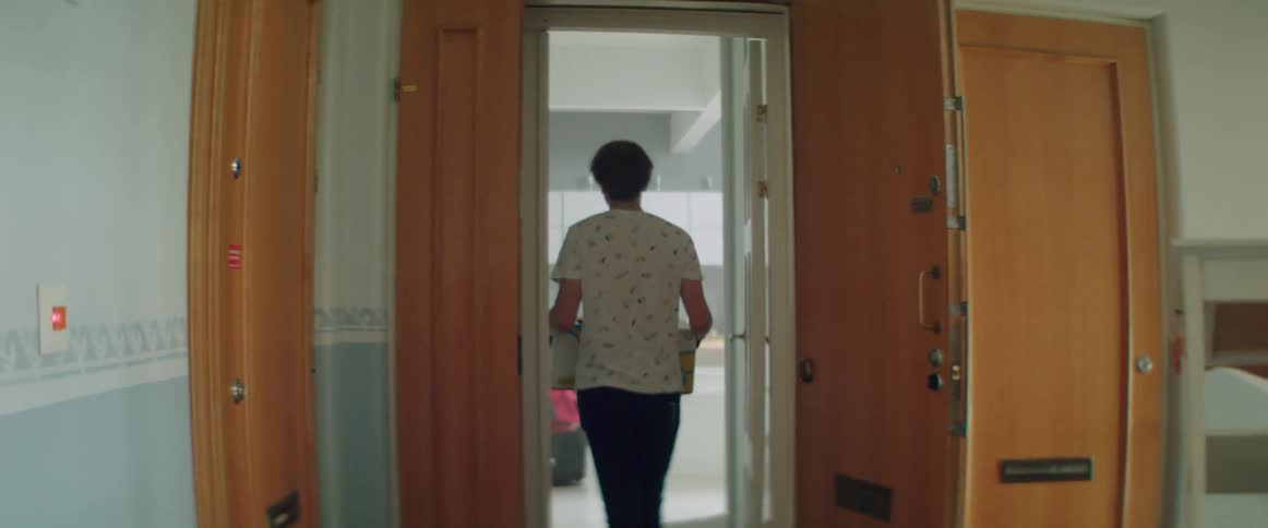 Rear view of a man carrying boxes into an apartment through front door.