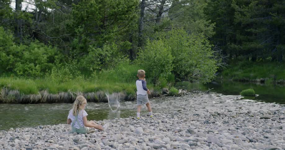 Two children throw rocks into a river