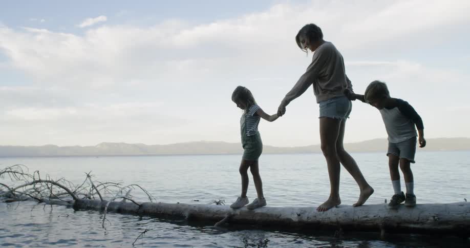 A woman and two children balance on a fallen tree in a lake