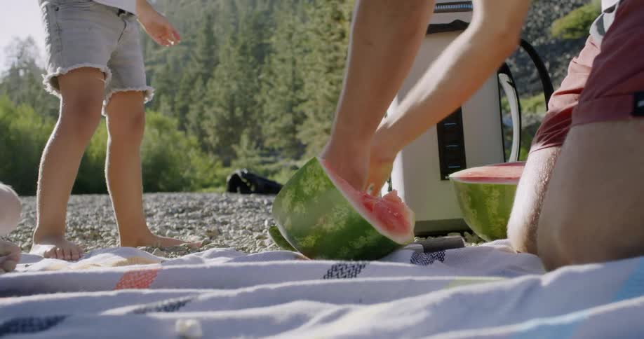 A man cuts a watermelon while picnicking