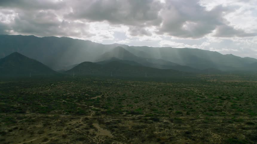 The sun is casting rays through clouds as they hang over a mountain range