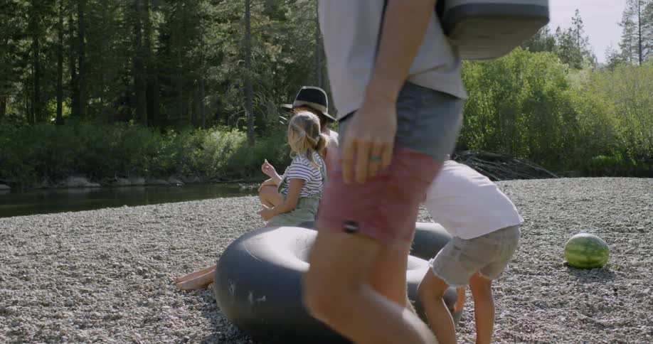A family are sitting on inner tubes next to a creek