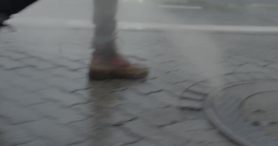 A person in jeans and boots walks briskly down a side walk in a city