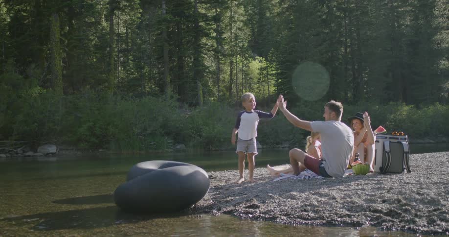 Man gives boy a high five near a stream on a cloudy day