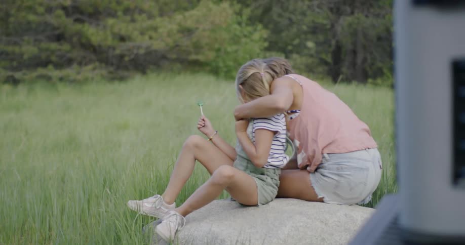 A mother and daughter sit on a rock in a grassy field