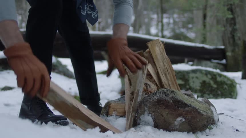 Man is chopping and stacking wood for fire in the snow
