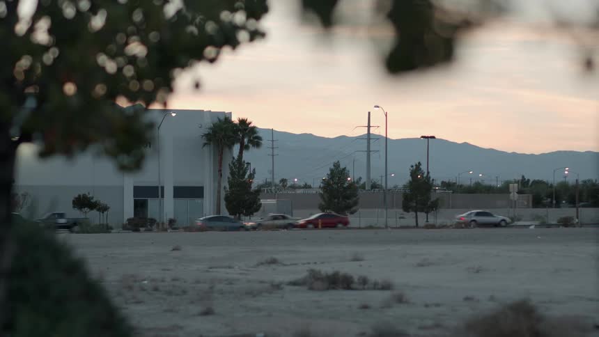 Cars travel on a street next to an empty lot at sunset