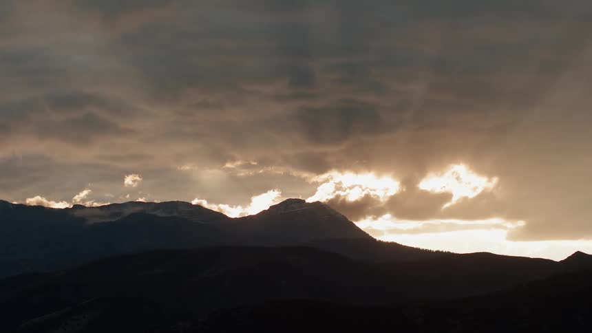 The sunlight reflects off the clouds as the sun sets behind the hill
