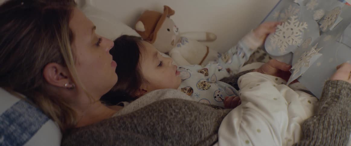 A woman reads a story to a young girl in bed