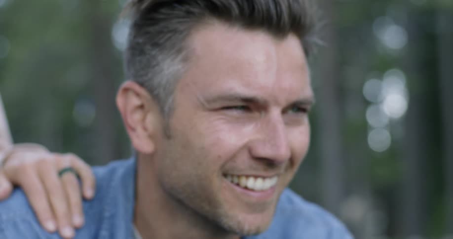 A man smiles squats down and holds his camera up to take a picture