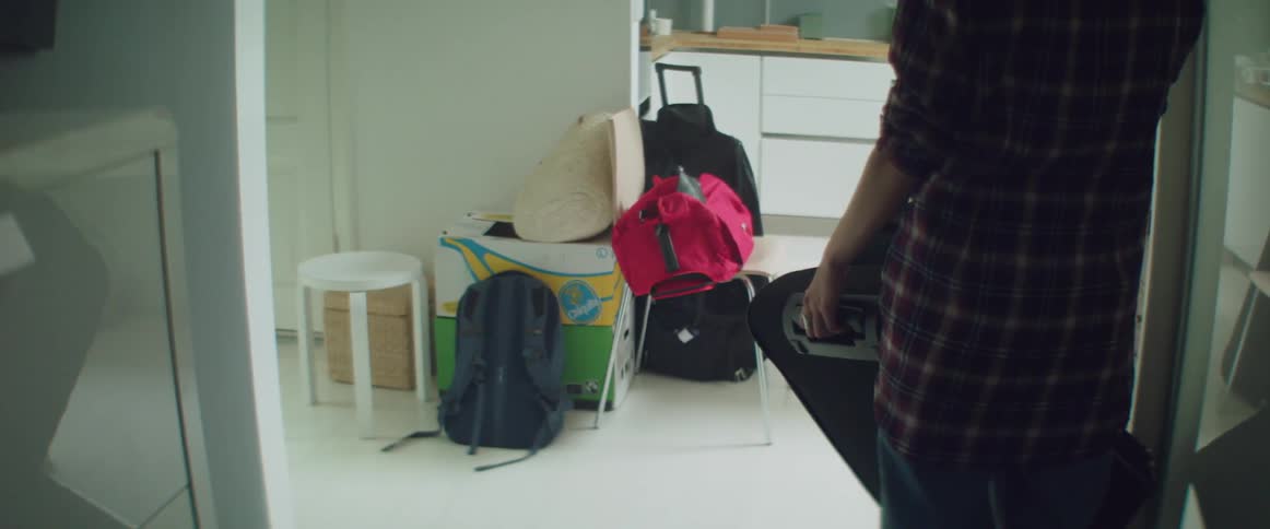 A person wearing a plaid shirt lifts a heavy suitcase during relocation.