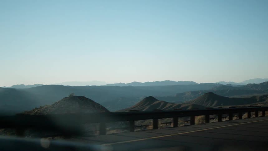 The road has a vast mountain range over the railing