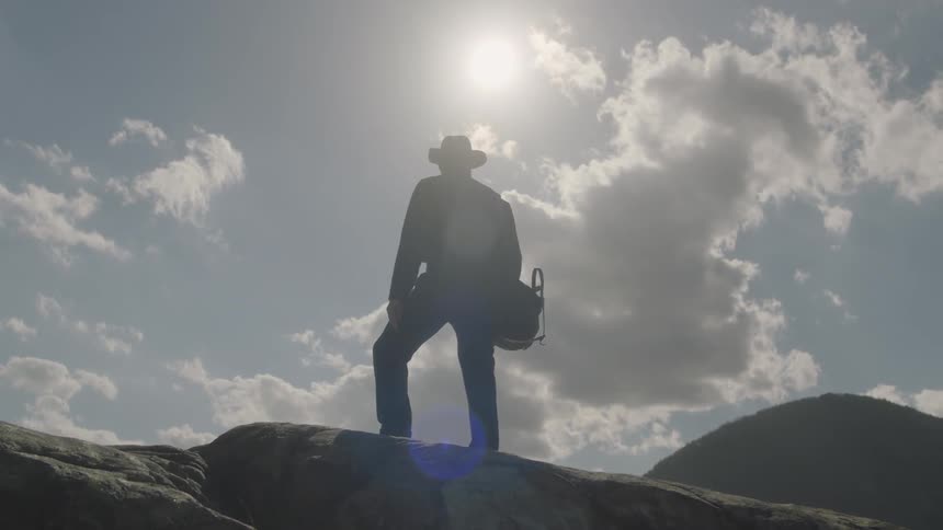 A man is standing on a boulder on a sunny day taking in the view