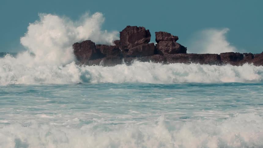 Oceans waves break and splash over rocks on shore