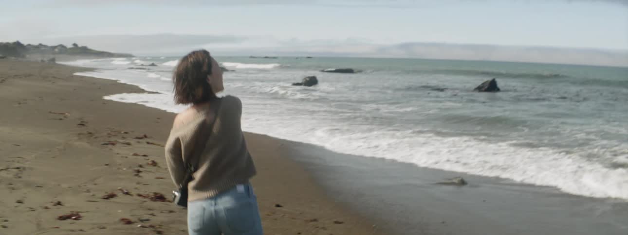 A woman is throwing stones into the ocean during the day