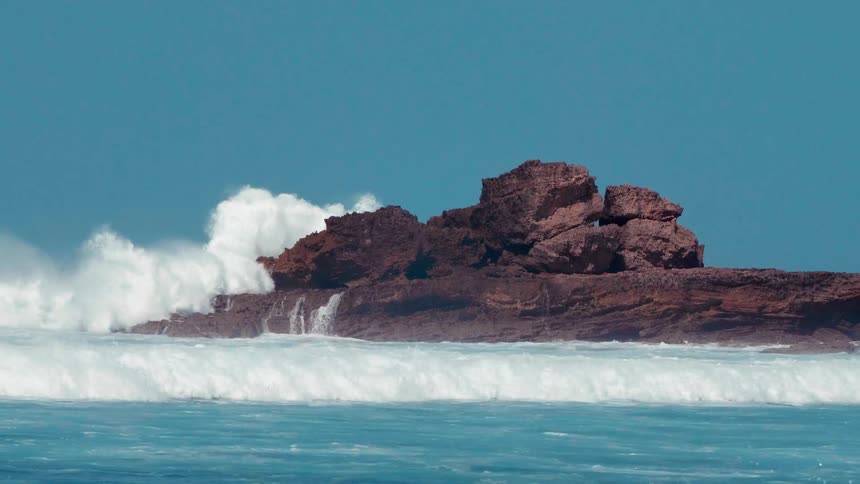 Large waves are crashing onto large rocks sticking out of the ocean