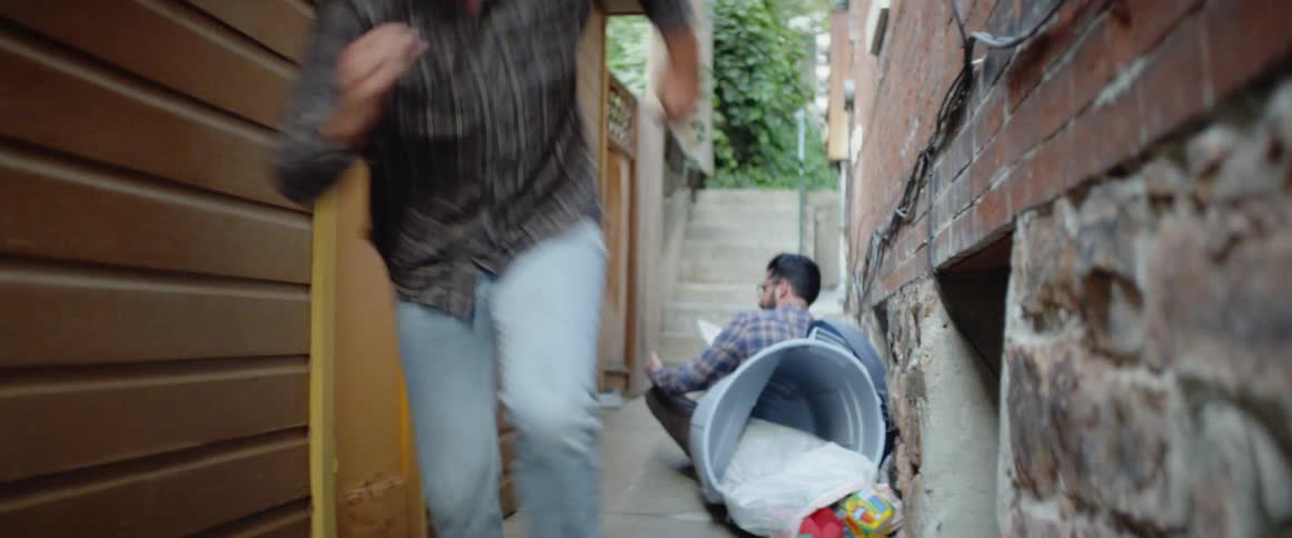 Man gets up and runs away from another man who is sitting in an alleyway