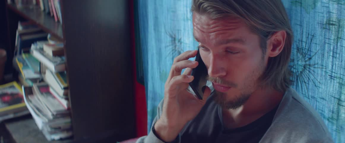 Man sitting in a room and talking on a cell phone sitting next to a window