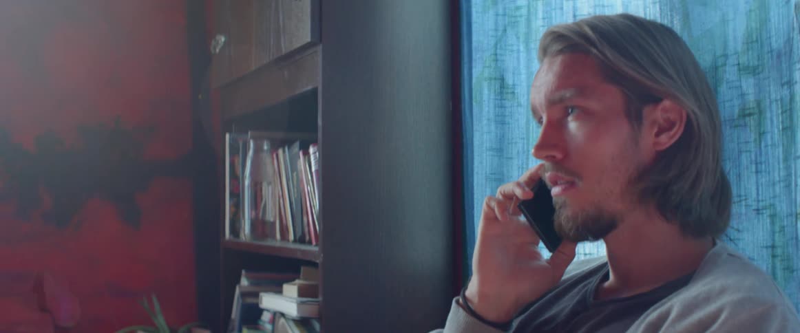 Close up view of a bearded man talking on smartphone near a bookshelf.