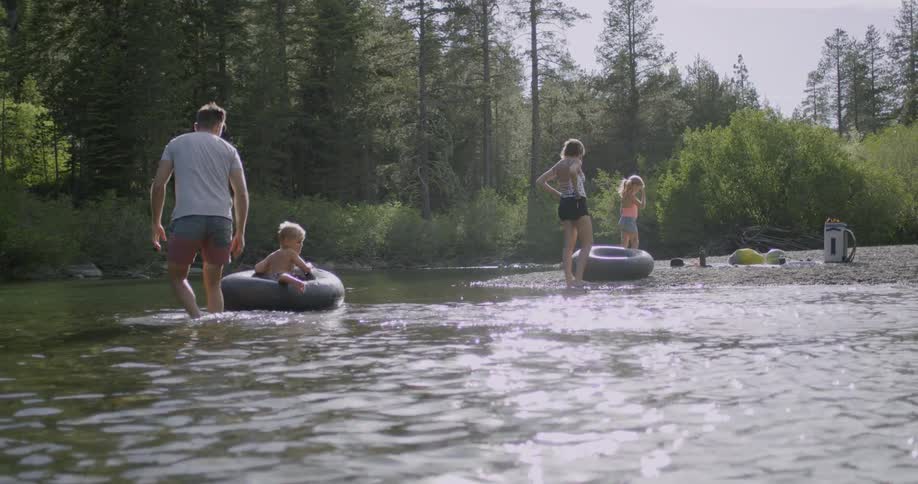 Parents watch as their children ride inner tubes in the stream