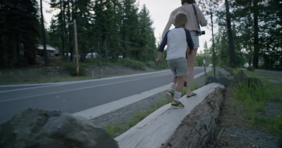 A mother and boy are marching on a tree trunk near a road at dusk