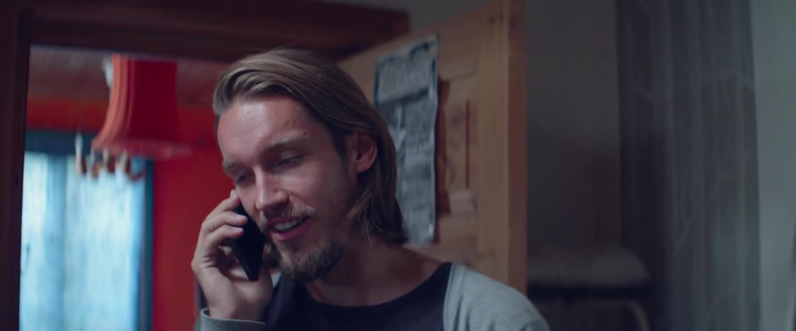 Close up of a man smiling gently while talking on smartphone at home.