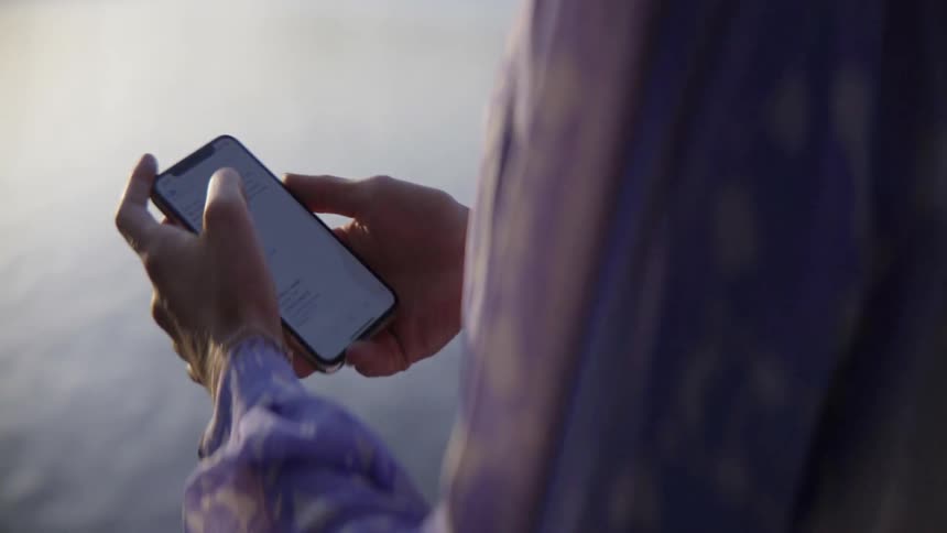 An emotional woman checks her device during a quiet walk by the shore.