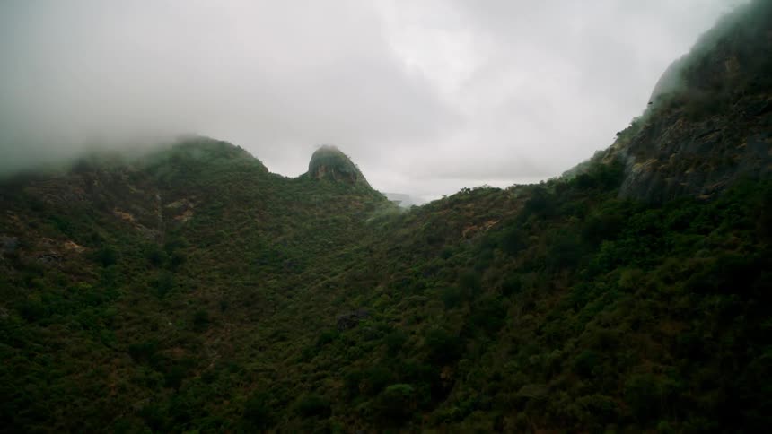 Clouds hang above a green tree covered mountain