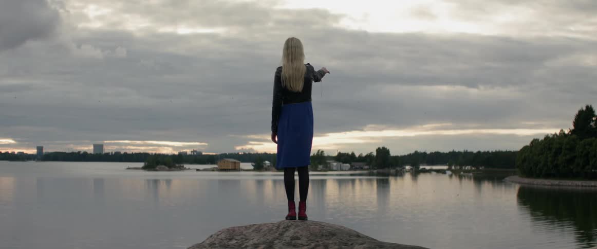 A solitary female traveler stands under a dramatic cloudy sky on summer evening.