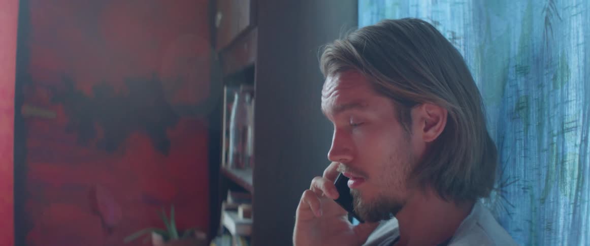 Man sitting in a room and talking on a cell phone sitting next to a window