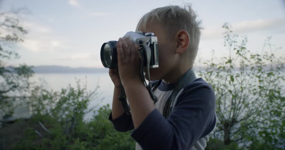 A young boy plays with a camera outside