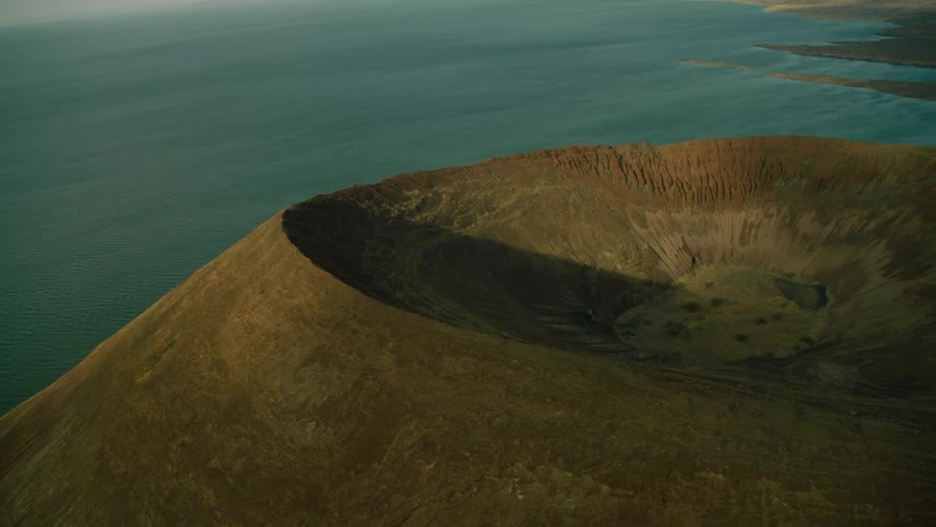A large crater sits on top of a large mountain next to the ocean